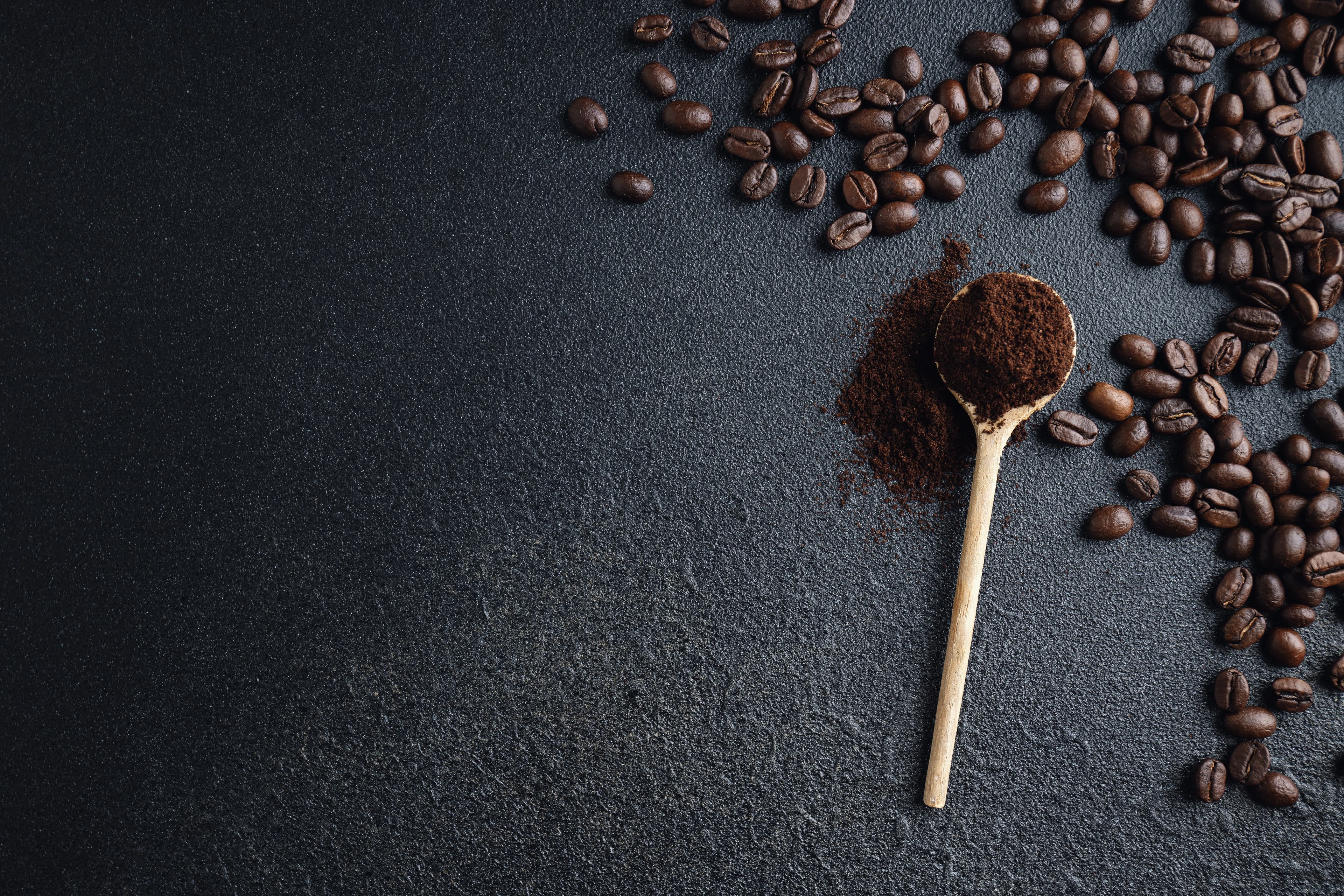 Kaffeebohnen und gemahlener Kaffee auf einem Löffel vor dunklem Hintergrund